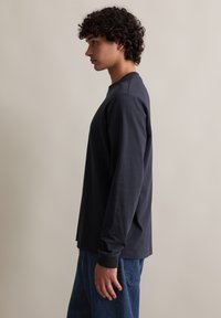 Granatowa bawełniana koszula z długim rękawem, okrągłym dekoltem i ściągaczami przy mankietach, w zestawieniu z luźnymi niebieskimi dżinsami. Gładka tekstura i prosty krój.