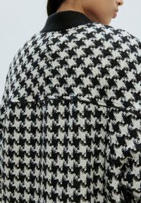 Schwarz-weißer Hahnentritt-Muster-Cardigan mit schwarzem geripptem Kragen, aus strukturiertem Stoff mit subtilen Nähten.