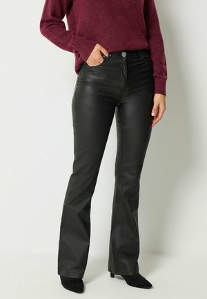 Personne portant un pantalon flare en cuir noir associé à un pull à manches longues bordeaux et des escarpins noirs pointus.