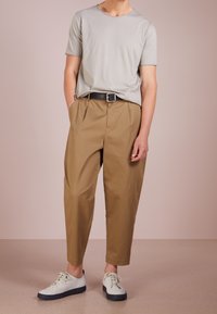 Lichtgrijs kortmouwen t-shirt gecombineerd met losse beige broek en witte sneakers met een marineblauwe zool, zwart riem accentueert.