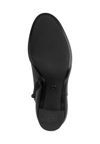 Semelle de chaussure en cuir noir montrant une semelle anti-dérapante striée et un petit talon avec le texte anti-glisse et un petit emblème en métal près de l'arche.