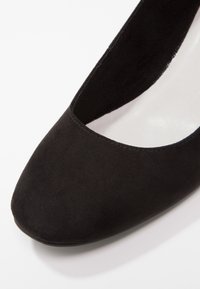 Escarpin en daim noir avec un bout rond, intérieur lisse et une légère brillance sur la semelle. Design simple et surface extérieure texturée.