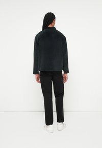 Mørk fløjlskjorte med en afslappet pasform, der har krave og lange ærmer, parret med sorte cargobukser og hvide sneakers.