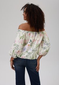Off-the-shoulder blomstertopp i lett stoff, med pastellfarger på kremfarget bakgrunn og puffede ermer. Brukt sammen med mørke jeans.