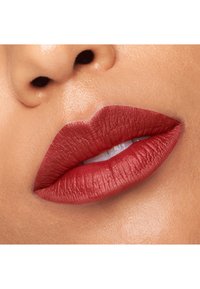 Rouge à lèvres mat et profond appliqué sur des lèvres lisses et pulpeuses, mettant en valeur des contours bien définis et une texture veloutée contre un teint clair.