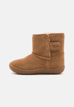 Bruine suède mid-kuitlaars met fleece voering, platte rubberen zool en UGG-logo op het zijlabel.