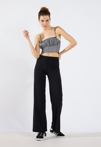 Sorte bredbenede bukser parret med en sort og hvid ternet cropped top med flæse detaljer og tynde stropper. Stylet med sorte snøresko.