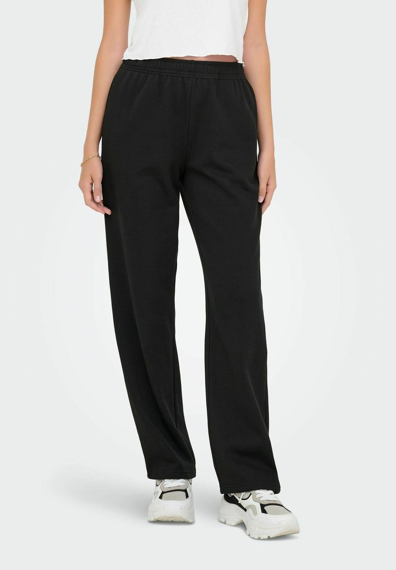 Zwarte joggingbroek met een elastische tailleband, losse pasvorm en gladde textuur, gecombineerd met witte sneakers en een cropped wit topje.