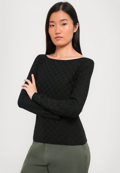 Top nero a maniche lunghe con un motivo geometrico testurizzato e scollo a barca, abbinato a pantaloni verde oliva.