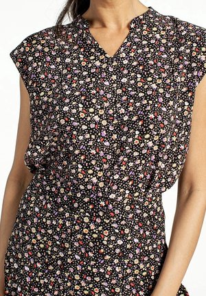 Woman wearing a sleeveless black dress with a small multicolored floral pattern and a short V-neck collar.