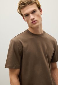 T-shirt marrone a girocollo realizzato in cotone, con maniche corte e una texture liscia, caratterizzato da un design semplice e dettagli di cucitura minimi.
