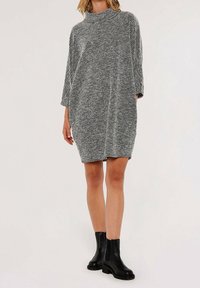 Tunique en tricot noir et blanc oversize avec col montant, manches trois-quarts et motif texturé, associée à des bottines noires à la cheville.