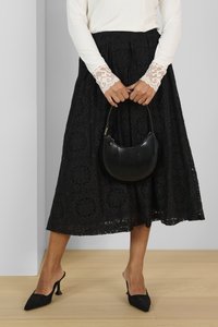 Svart spetskjol med texturerat blommönster, kombinerad med en vit långärmad topp med spetskant. Svart handväska och klackar fulländar looken.