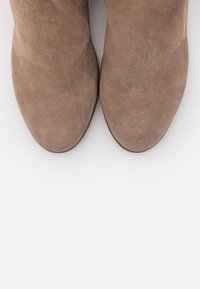 Un par de botas de ante de color marrón claro con punteras redondeadas vistas desde arriba sobre un fondo blanco.