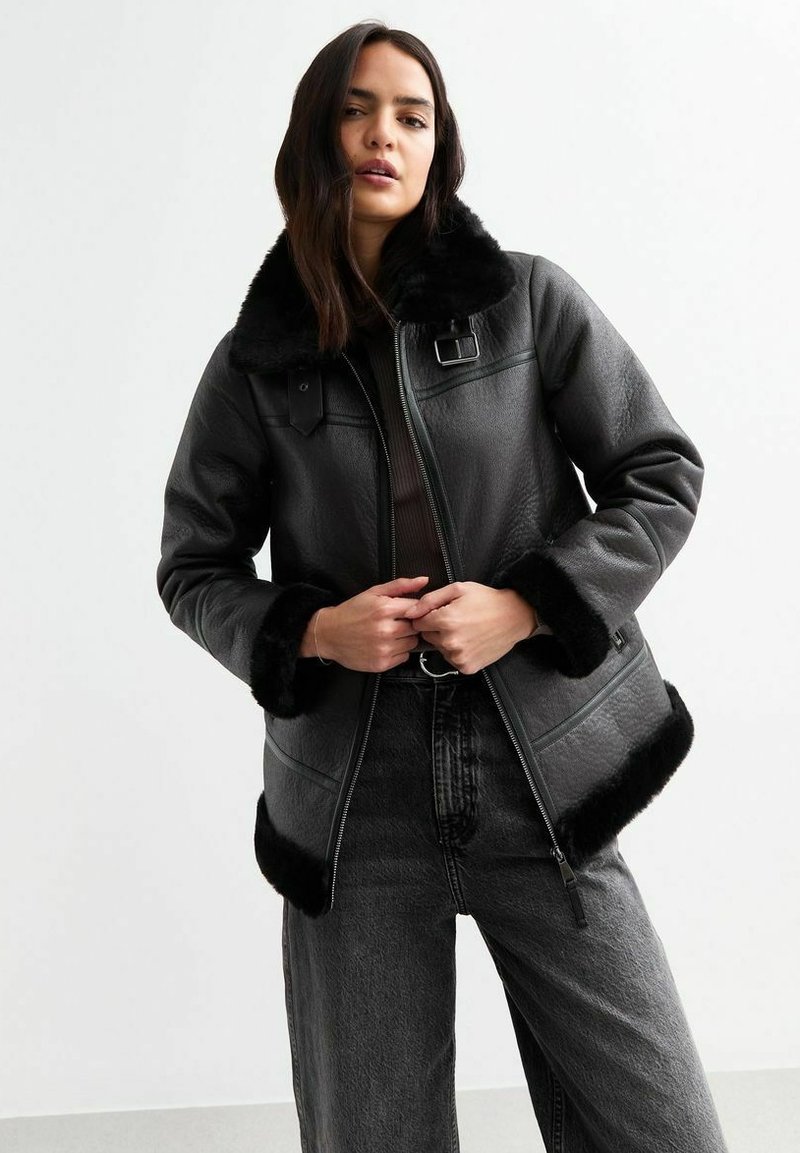 Zwarte leren jas met zachte faux fur kraag en manchetten, ritssluiting en zijzakken. Gecombineerd met hoge zwarte denim broek.