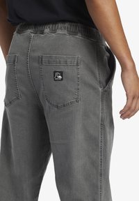 Gray denim pants with an elastic waistband, back pockets, and a logo patch near the right pocket. Smooth texture, relaxed fit.