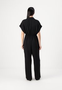 Combinaison noire à manches courtes avec une taille cintrée. Caractérisée par des jambes larges et une texture lisse. Design minimaliste, sans motifs ni accents visibles.