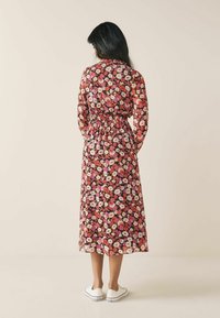 Robe midi fleurie à manches longues, taille cintrée, dans des tons de rose, rouge et blanc sur un fond sombre, associée à des baskets blanches.