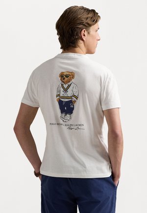 Hvit bomull t-skjorte med et detaljert illustrert bjørn som har solbriller og sporty antrekk på baksiden; inkluderer teksten "Polo Bear by Ralph Lauren".