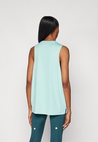 Top atlético sin mangas de color azul claro con un corte holgado, cuello redondo y aberturas laterales, combinado con leggings verde oscuro con puntos blancos.