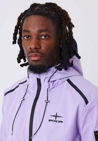 Veste légère violette avec capuche, arborant des accents noirs et un logo. Fabriquée en tissu lisse et léger avec un système de fermeture à cordon.