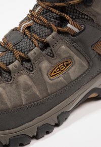 Wanderschuh mit einem robusten grauen Obermaterial aus Synthetik, verstärkter Zehenkappe, orangefarbenen Akzenten, strukturiertem Mesh-Futter und einer langlebigen Profilsohle.
