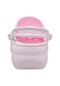 Sabots Crocs roses avec un extérieur lisse, une base texturée, une sangle arrière et des accents perle sur la sangle. Design simple et arrondi.