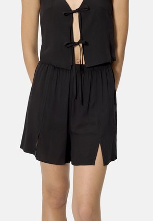 Top negro sin mangas con dos lazos delanteros combinado con shorts negros de talle alto con cinturilla elástica y aberturas delanteras en cada pierna.