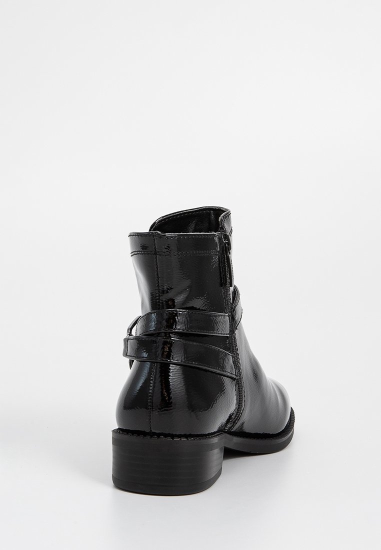 Stivaletti neri alla caviglia con finitura lucida in vernice, punta rotonda, chiusura con zip e dettaglio di doppia cinghia intorno alla caviglia. Tacco basso impilato.