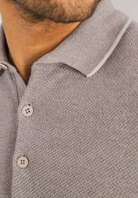 Grijze gebreide polo met een textuurstof, drie lichtgekleurde knopen en een contrasterende witte bies langs de kraag.