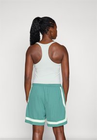 Top deportivo de color verde claro con diseño de espalda nadadora, combinado con pantalones cortos en tono aguamarina que presentan tiras laterales blancas y una cinturilla elástica.