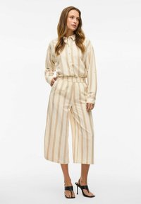 Krēmu krāsas, svītrains krekls un platās bikses ar brīvu piegriezumu. Svītrās ir rusu akcenti. Kombinēts ar melnām kurpēm uz papēžiem.