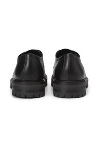 Schwarze Lederschuhe mit abgerundetem Zehenbereich und tiefer Ferse. Die Sohle ist klobig und strukturiert, mit horizontalen Streifen für zusätzlichen Halt.