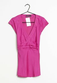 Pink dress with a V-neck and short sleeves, featuring pleated detailing at the waist. Made of smooth fabric, it hangs on a black hook.