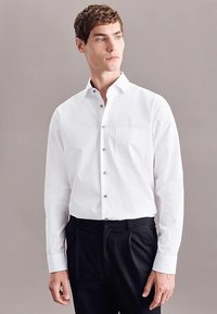 Camicia bianca abbottonata con tasca, caratterizzata da un colletto classico e bottoni argentati, abbinata a pantaloni neri. Tessuto dalla trama liscia.