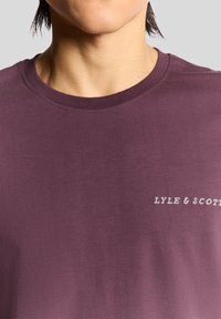 Short-sleeve, crew neck T-shirt in dark purple fabric, featuring "LYLE & SCOTT" embroidered in white on the left chest area. Smooth texture.
