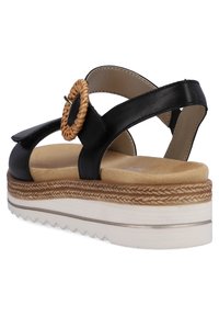 Sandales à plateforme en cuir noir avec un accent circulaire tissé, semelle intérieure beige et semelle extérieure texturée. Les brides ajustables améliorent l'ajustement et le confort.