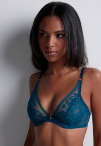 Soutien-gorge en dentelle teal avec un design de bonnets triangulaires, des motifs floraux brodés, des bretelles ajustables et des accents en métal doré.