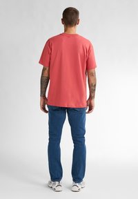 Rode katoenen T-shirt met korte mouwen en een ontspannen pasvorm, gedragen met blauwe jeans en sneakers, met een eenvoudige achterkant.