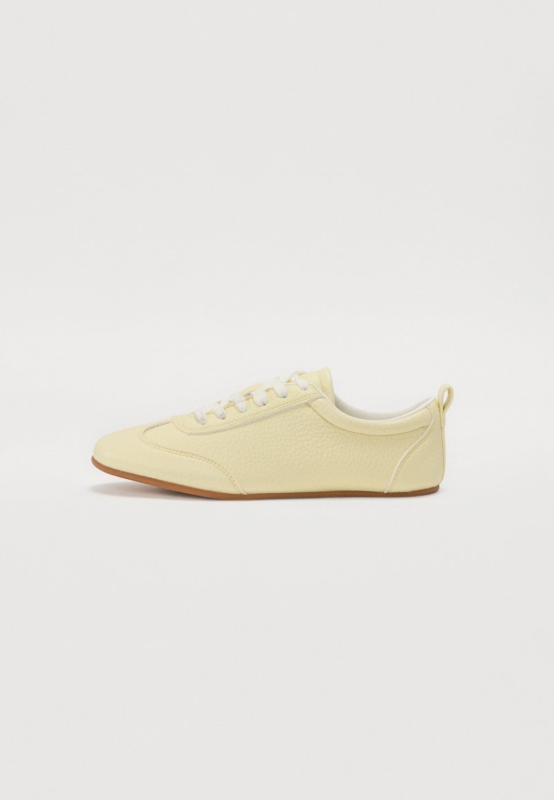 Baskets basses beige clair avec lacets blancs, matériau texturé et semelle en caoutchouc, vues de côté sur fond blanc.