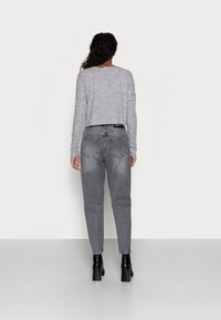 Grå kortärmad tröja och grå jeans med hög midja. Tröjan har en strukturerad stickning; jeansen har en blekt finish och vanliga fickor. Svarta klackstövlar.