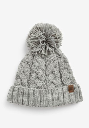 Grå kabelstickad mössa med ribbad uppvikning, prydd med en fluffig pom-pom. Har en liten brun läderlogg i sidan.