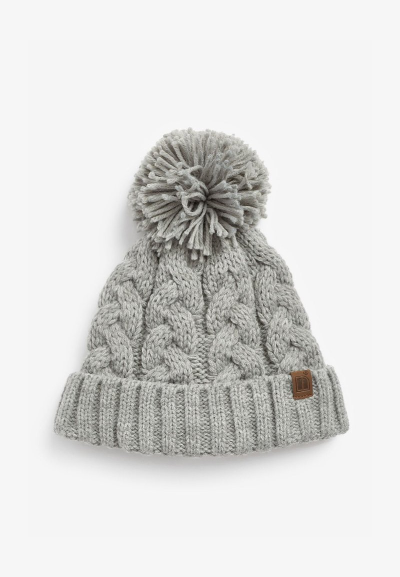 Pilko megzto audinio beanie su raštuotu apvadu, viršuje papuoštas pūkuotu pom-pomu. Šone yra mažas rudas odinis logotipo ženkliukas.