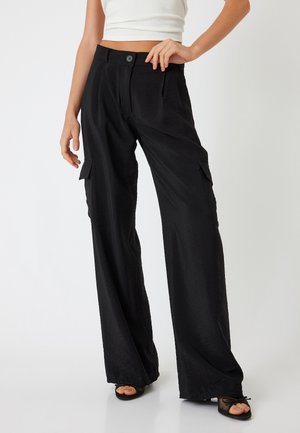 Zwarte cargobroek met wijde pijpen en een gestructureerde afwerking, met zijzakken en een knoopsluiting bij de taille, gestyled met een aansluitend wit topje.