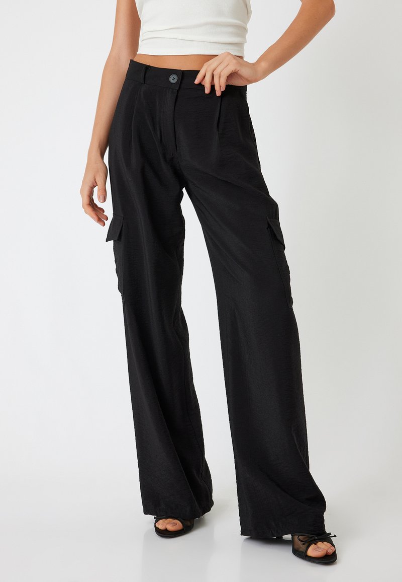 Zwarte cargobroek met wijde pijpen en een gestructureerde afwerking, met zijzakken en een knoopsluiting bij de taille, gestyled met een aansluitend wit topje.