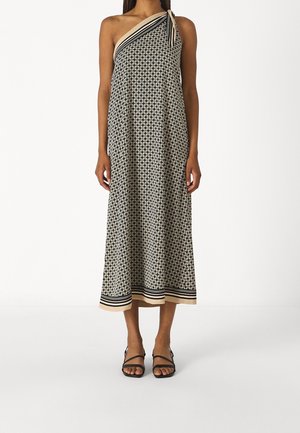 Mujer con un vestido midi de un solo hombro con estampado en negro y beige, con detalle de lazo y sandalias negras con tiras.