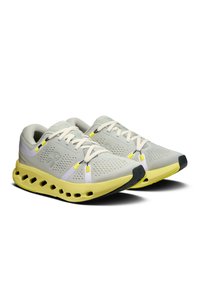 Baskets de sport gris clair avec une tige en mesh, des accents jaunes et une semelle rembourrée dotée de sections découpées pour une meilleure respirabilité.