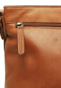 Tan leather bag corner with visible zipper and stitched leather pull tab on a close-up view.