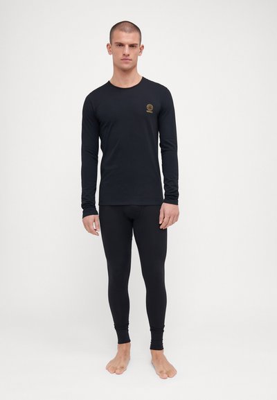 Maglia termica nera a maniche lunghe e leggings aderenti realizzati in materiale liscio, con un piccolo logo dorato sul petto. Design minimalista.
