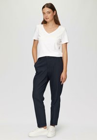 T-shirt en coton blanc à col en V associée à un pantalon bleu marine slim et des baskets blanches. Design simple avec peu de détails.